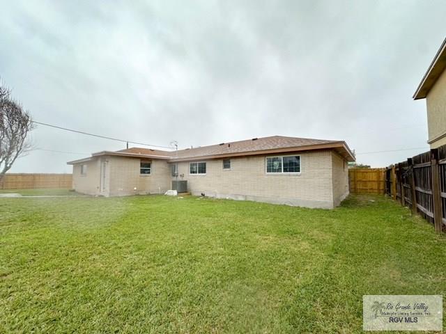 back of property featuring brick siding, a lawn, a fenced backyard, and central air condition unit