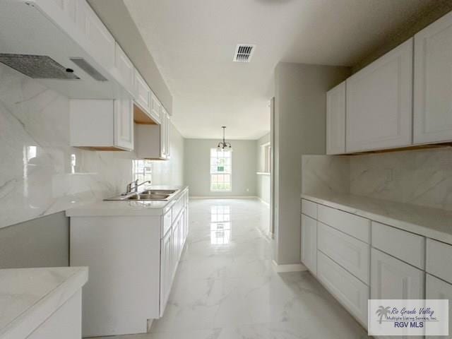 kitchen with tasteful backsplash, visible vents, marble finish floor, white cabinetry, and a sink