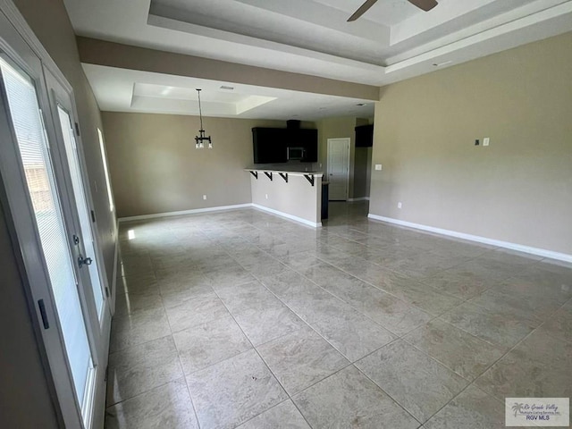 unfurnished living room featuring ceiling fan with notable chandelier and a raised ceiling