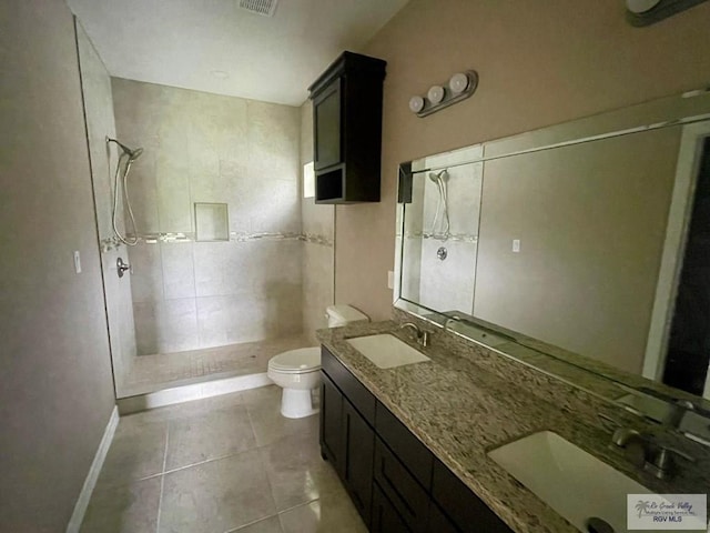 bathroom featuring tile patterned flooring, a tile shower, vanity, and toilet