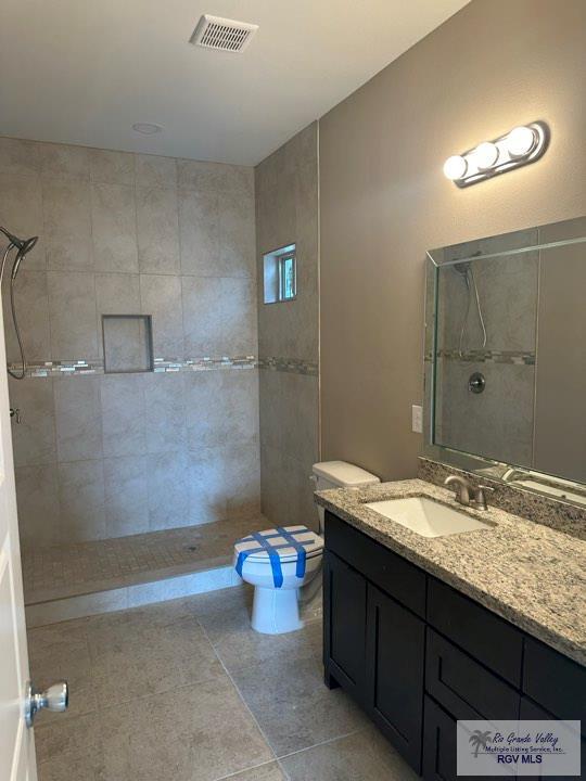 bathroom with tile patterned flooring, vanity, toilet, and tiled shower