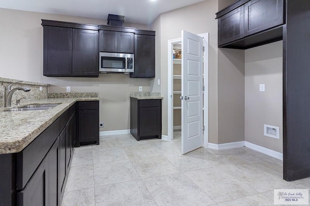 kitchen with light stone counters, sink, light tile patterned flooring, and dark brown cabinets