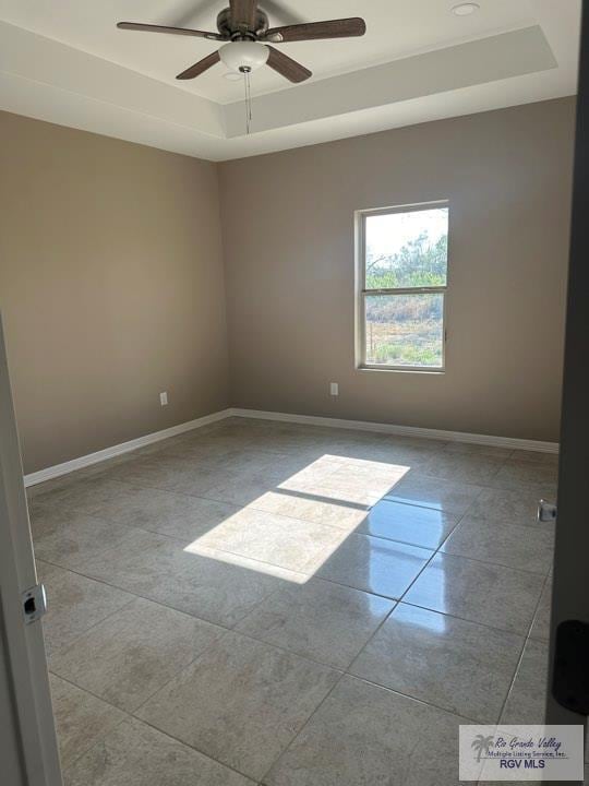 tiled spare room featuring a tray ceiling and ceiling fan