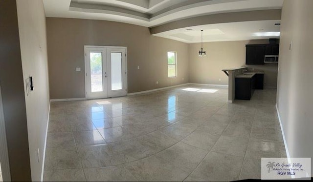 tiled empty room featuring a chandelier, french doors, and a tray ceiling