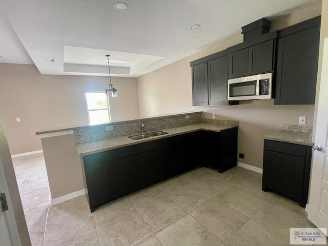 kitchen with kitchen peninsula, light stone counters, a raised ceiling, sink, and pendant lighting