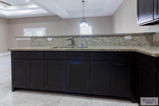 kitchen with an inviting chandelier, light stone countertops, sink, and a tray ceiling