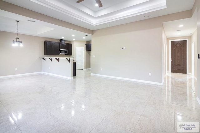 unfurnished living room featuring a tray ceiling and ceiling fan