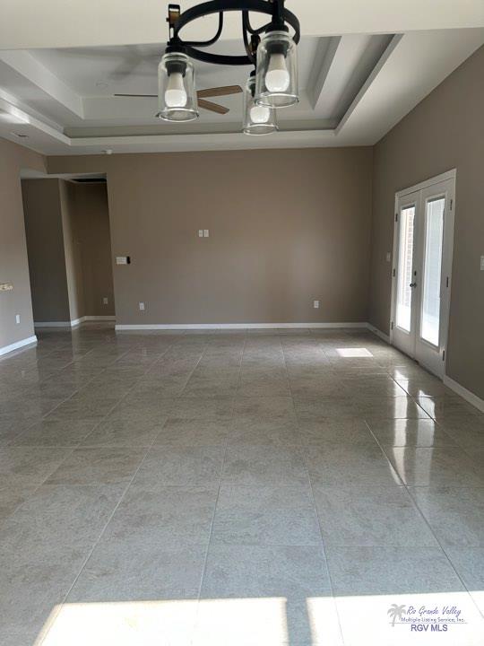 empty room featuring french doors, a tray ceiling, and ceiling fan