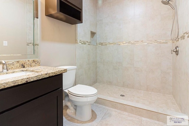 bathroom with tiled shower, tile patterned floors, vanity, and toilet