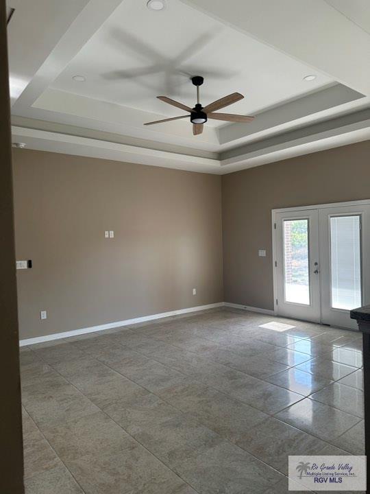 unfurnished room with ceiling fan, a raised ceiling, and french doors