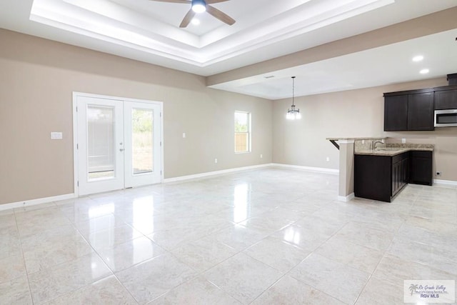 interior space featuring ceiling fan, french doors, a raised ceiling, light stone counters, and kitchen peninsula