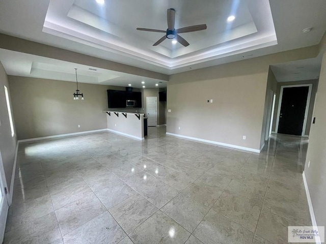 unfurnished living room with ceiling fan with notable chandelier and a raised ceiling