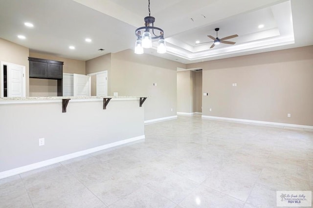 interior space featuring a raised ceiling and ceiling fan with notable chandelier