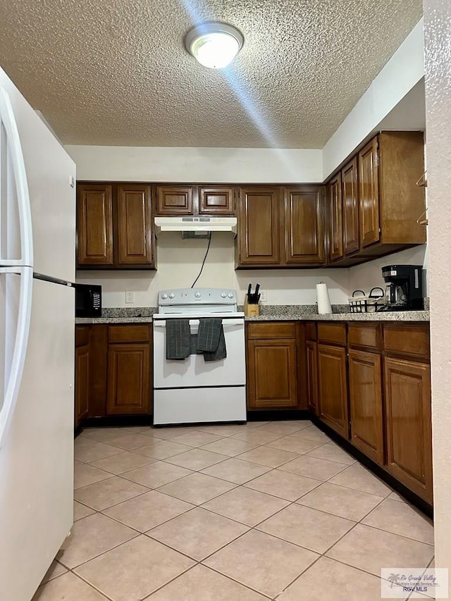 kitchen featuring a textured ceiling, light stone counters, light tile patterned flooring, and white appliances