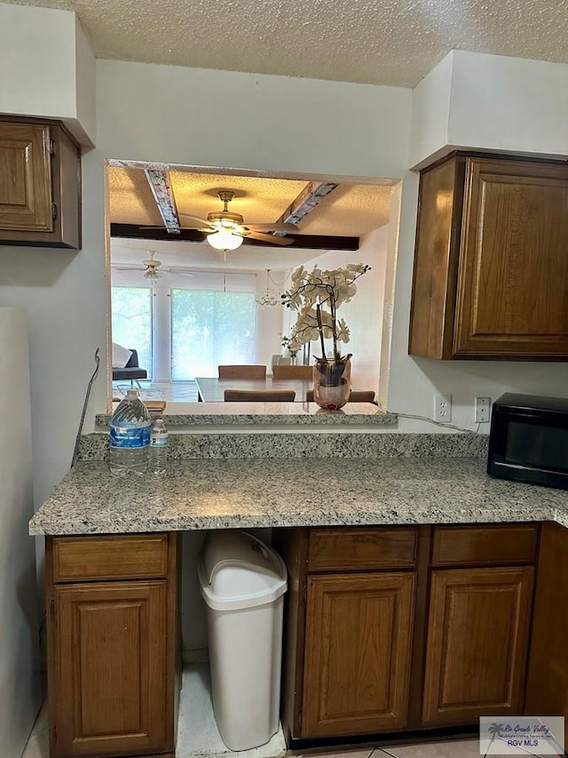 kitchen with ceiling fan, light stone countertops, and a textured ceiling