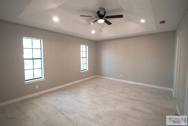 empty room with ceiling fan, a tray ceiling, visible vents, recessed lighting, and baseboards