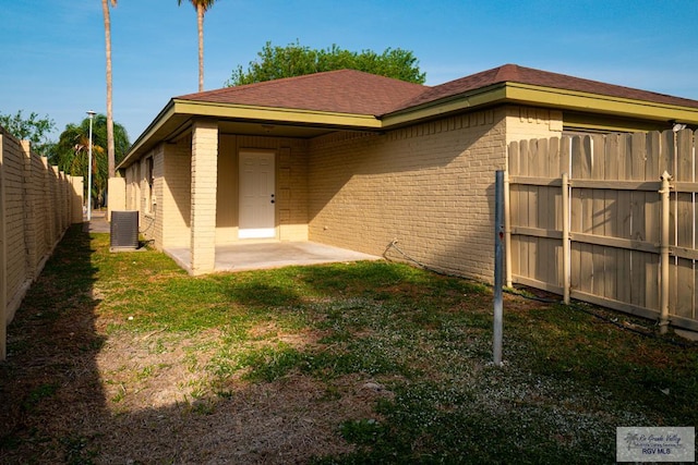 rear view of property featuring a lawn, a fenced backyard, central AC, and brick siding