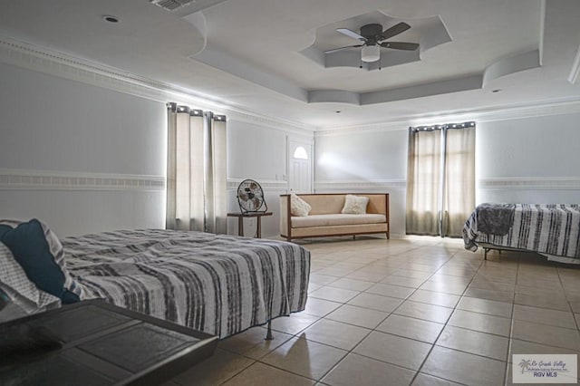 bedroom featuring light tile patterned floors, a raised ceiling, crown molding, and a wainscoted wall