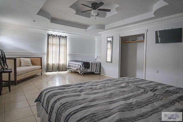 bedroom featuring a tray ceiling, a closet, ornamental molding, a ceiling fan, and light tile patterned flooring