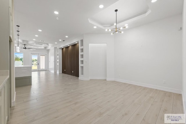 unfurnished living room featuring a tray ceiling, french doors, light hardwood / wood-style floors, and ceiling fan with notable chandelier