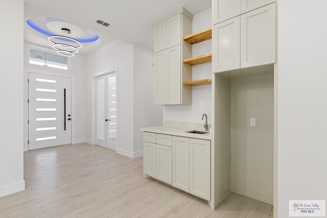 kitchen featuring an inviting chandelier, light hardwood / wood-style floors, white cabinetry, and sink