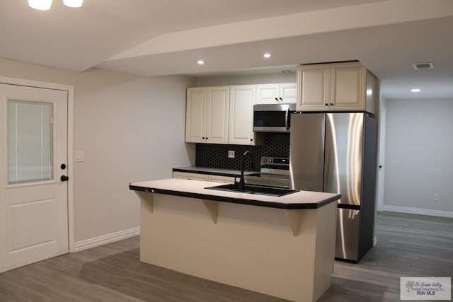 kitchen featuring dark wood-type flooring, a center island with sink, sink, appliances with stainless steel finishes, and tasteful backsplash