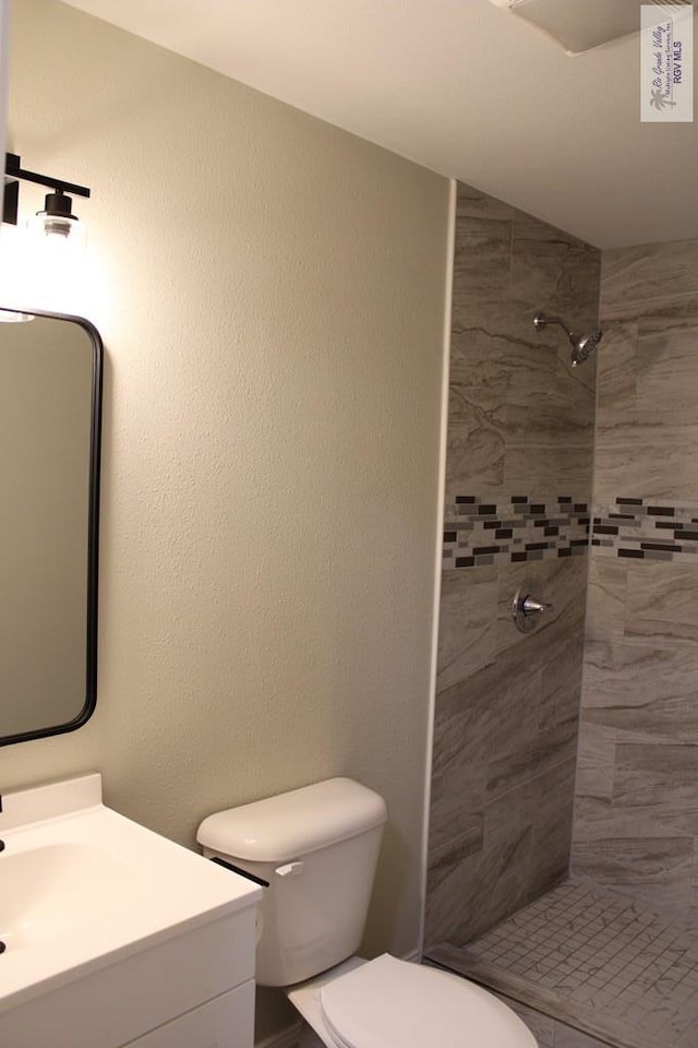 bathroom with a tile shower, vanity, and toilet