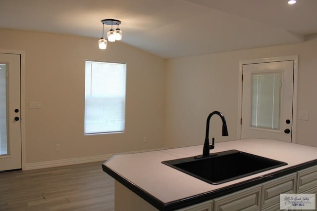 kitchen featuring vaulted ceiling, sink, light hardwood / wood-style floors, white cabinetry, and hanging light fixtures