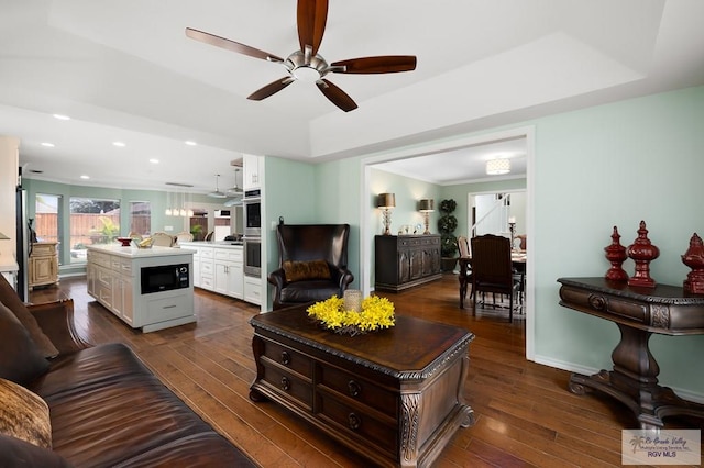 living room featuring dark hardwood / wood-style flooring, a tray ceiling, and ceiling fan