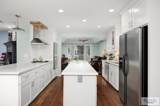 kitchen featuring wall chimney exhaust hood, stainless steel appliances, ceiling fan, dark wood-type flooring, and white cabinetry