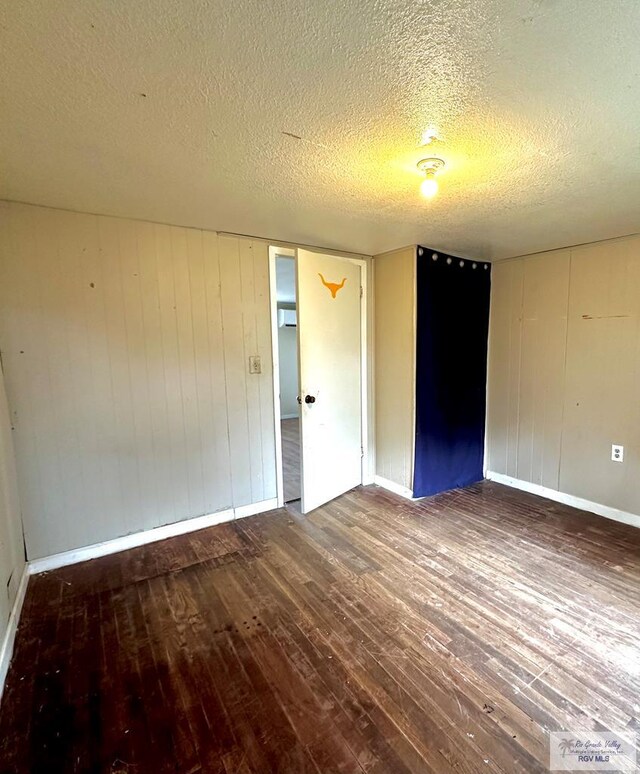 spare room with a textured ceiling, ceiling fan, wooden walls, cooling unit, and wood-type flooring