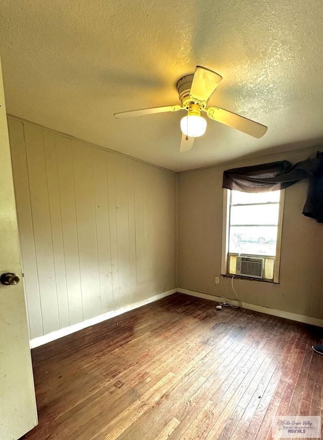 spare room featuring ceiling fan, wood walls, cooling unit, wood-type flooring, and a textured ceiling