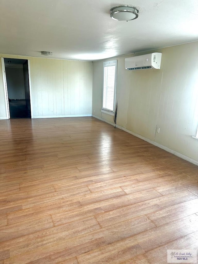 spare room with light hardwood / wood-style flooring, an AC wall unit, and wood walls