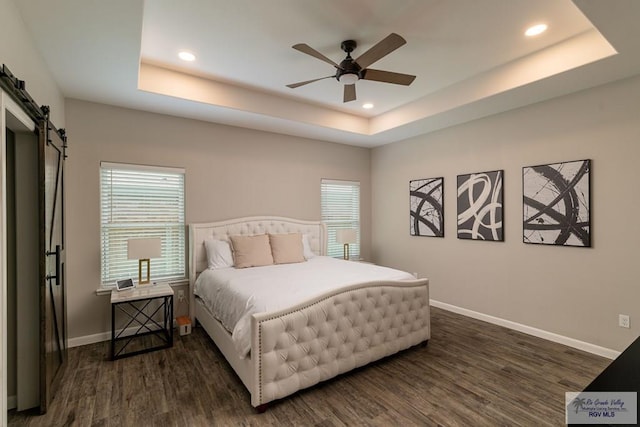 bedroom featuring dark hardwood / wood-style floors, a barn door, a raised ceiling, and ceiling fan