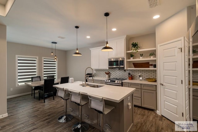 kitchen with sink, dark wood-type flooring, stainless steel appliances, an island with sink, and decorative light fixtures