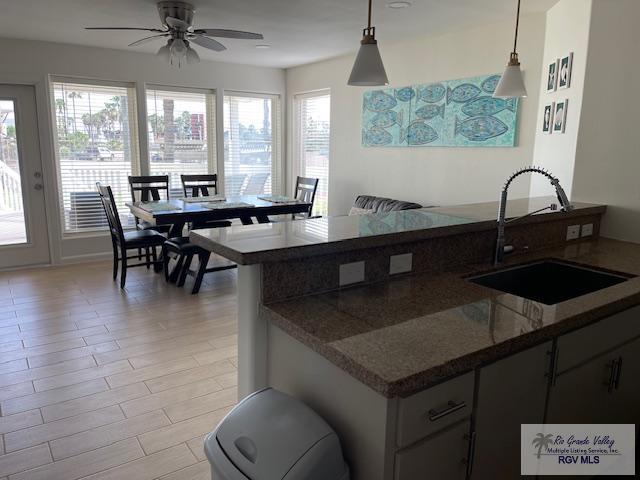 kitchen featuring kitchen peninsula, light wood-type flooring, ceiling fan, sink, and pendant lighting