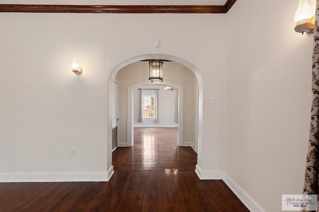 hallway featuring baseboards, arched walkways, dark wood-type flooring, and crown molding