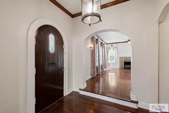 foyer featuring ceiling fan, ornamental molding, a fireplace, wood finished floors, and arched walkways