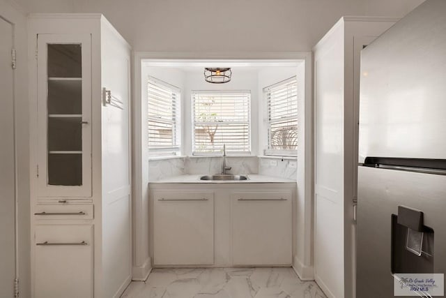 kitchen with light countertops, freestanding refrigerator, marble finish floor, white cabinetry, and a sink