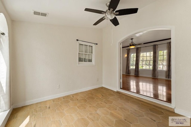 unfurnished room with visible vents, arched walkways, baseboards, and a ceiling fan