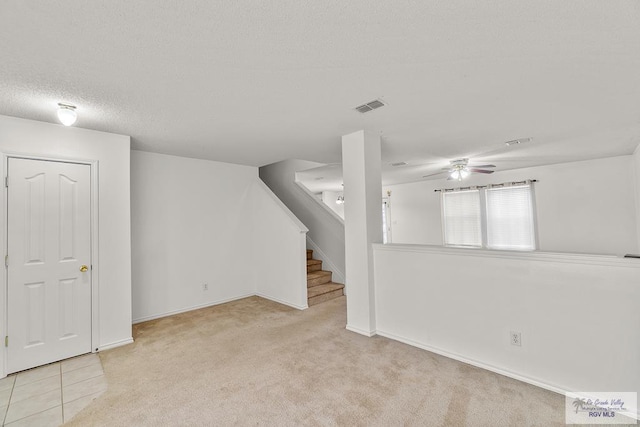 basement with a textured ceiling, light colored carpet, and ceiling fan