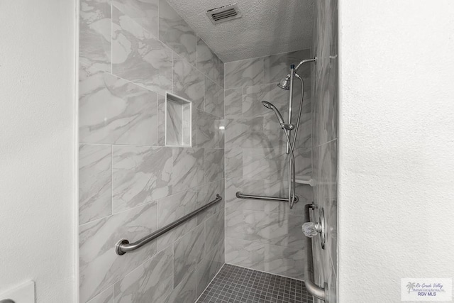 bathroom with a tile shower and a textured ceiling