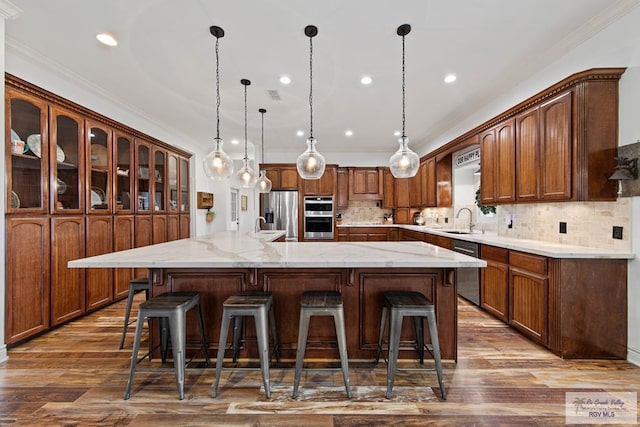 kitchen with appliances with stainless steel finishes, tasteful backsplash, a spacious island, sink, and decorative light fixtures