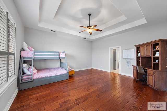 bedroom with a tray ceiling, ceiling fan, and dark wood-type flooring