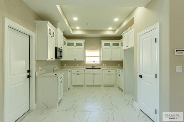 kitchen featuring marble finish floor, black microwave, a raised ceiling, and a sink