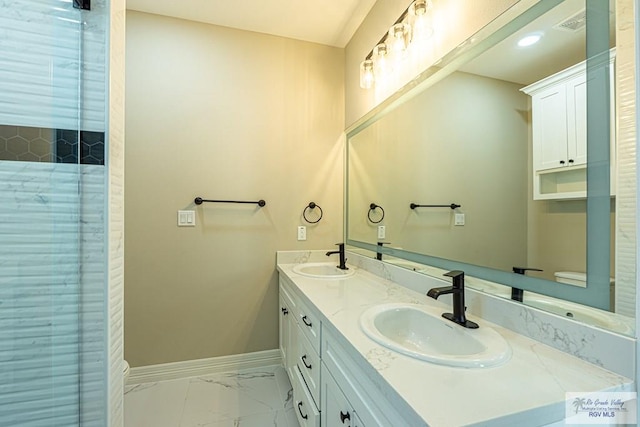 full bath with double vanity, marble finish floor, baseboards, and a sink