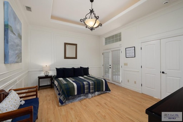 bedroom with light wood-type flooring, a raised ceiling, and a decorative wall