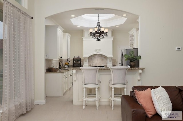 kitchen featuring a tray ceiling, tasteful backsplash, ornamental molding, white cabinets, and light stone countertops