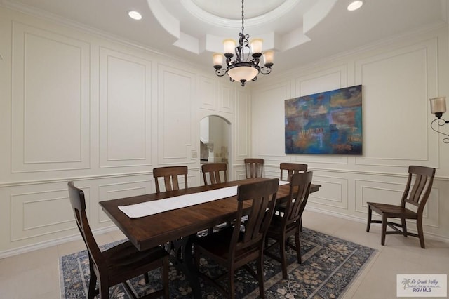 dining area featuring arched walkways, recessed lighting, a decorative wall, a tray ceiling, and an inviting chandelier