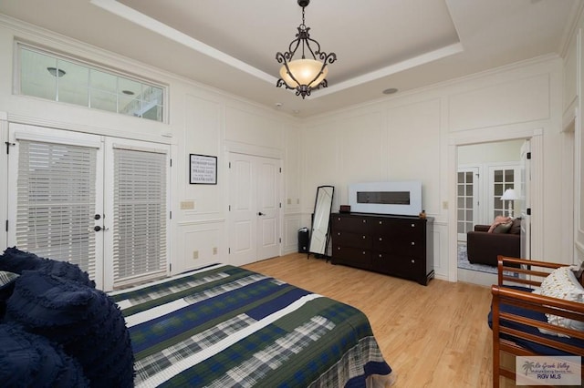 bedroom featuring crown molding, a raised ceiling, a decorative wall, and light wood-style flooring